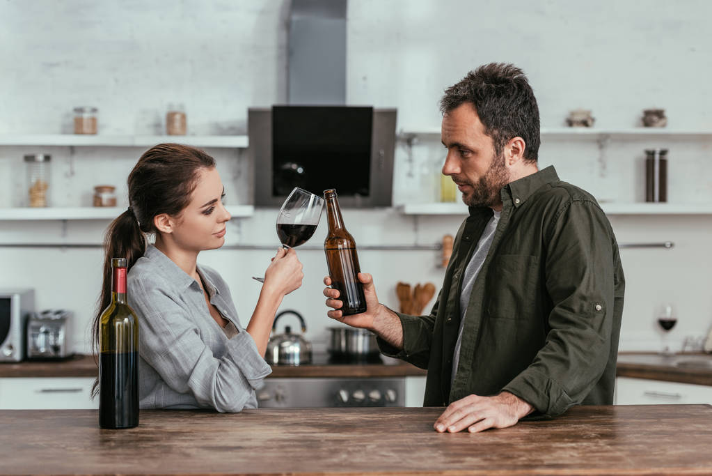 Couple with wine and beer clinking at kitchen - Photo, Image
