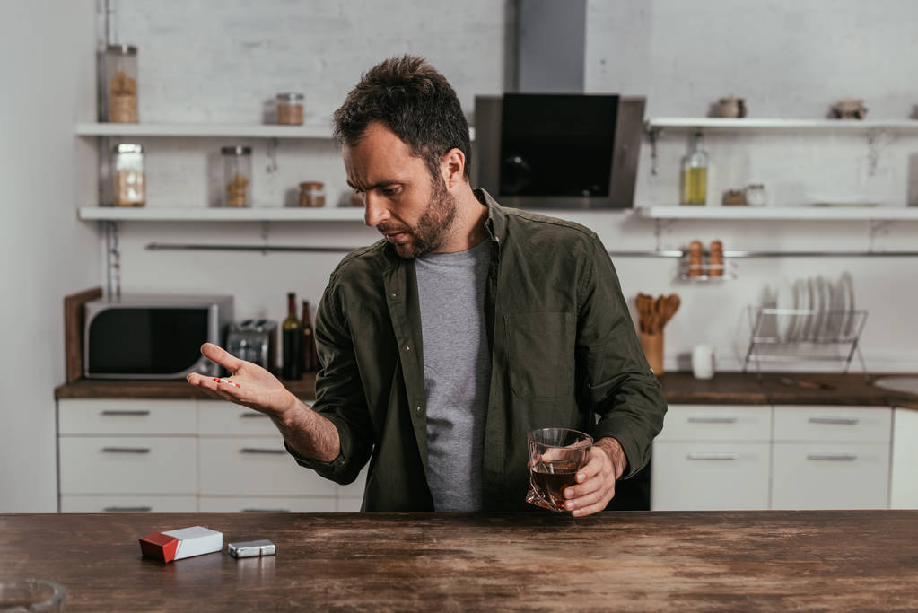 Man met whiskey glas holding pillen op keuken - Foto, afbeelding