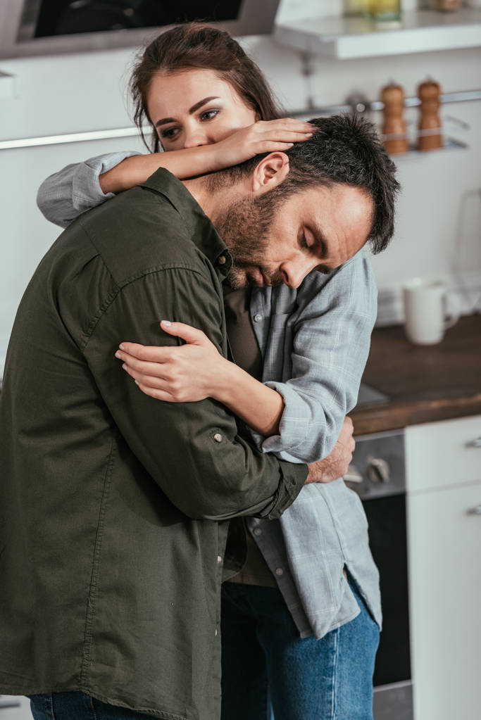 Woman hugging worried husband with alcohol addiction on kitchen - Photo, Image