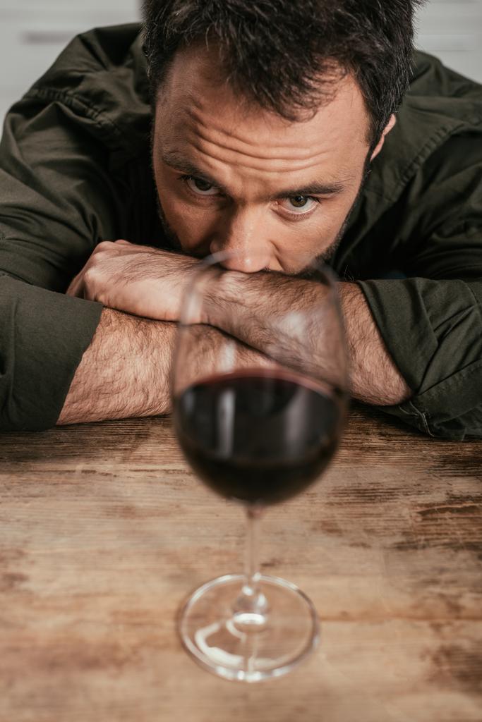 Selective focus of alcohol addicted man looking at wine glass on table - Photo, Image