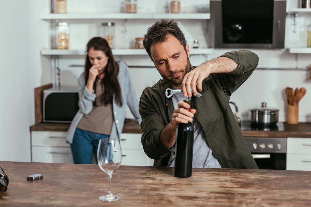 Επιλεκτική εστίαση του ανθρώπου άνοιγμα μπουκάλι κρασί και ανησυχούν σύζυγος στην κουζίνα - Φωτογραφία, εικόνα