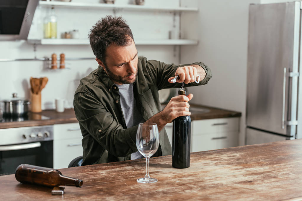 Hombre adicto al alcohol abriendo botella de vino en la cocina
 - Foto, Imagen