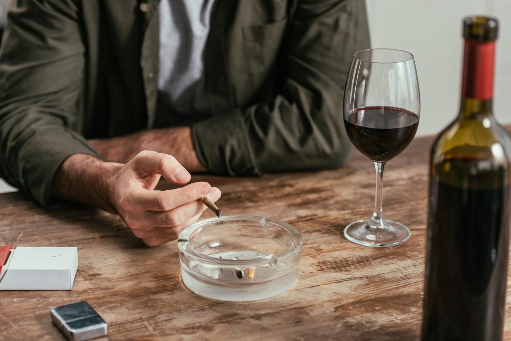 Vista recortada del hombre fumando cigarrillo junto a la copa de vino en la mesa
 - Foto, Imagen