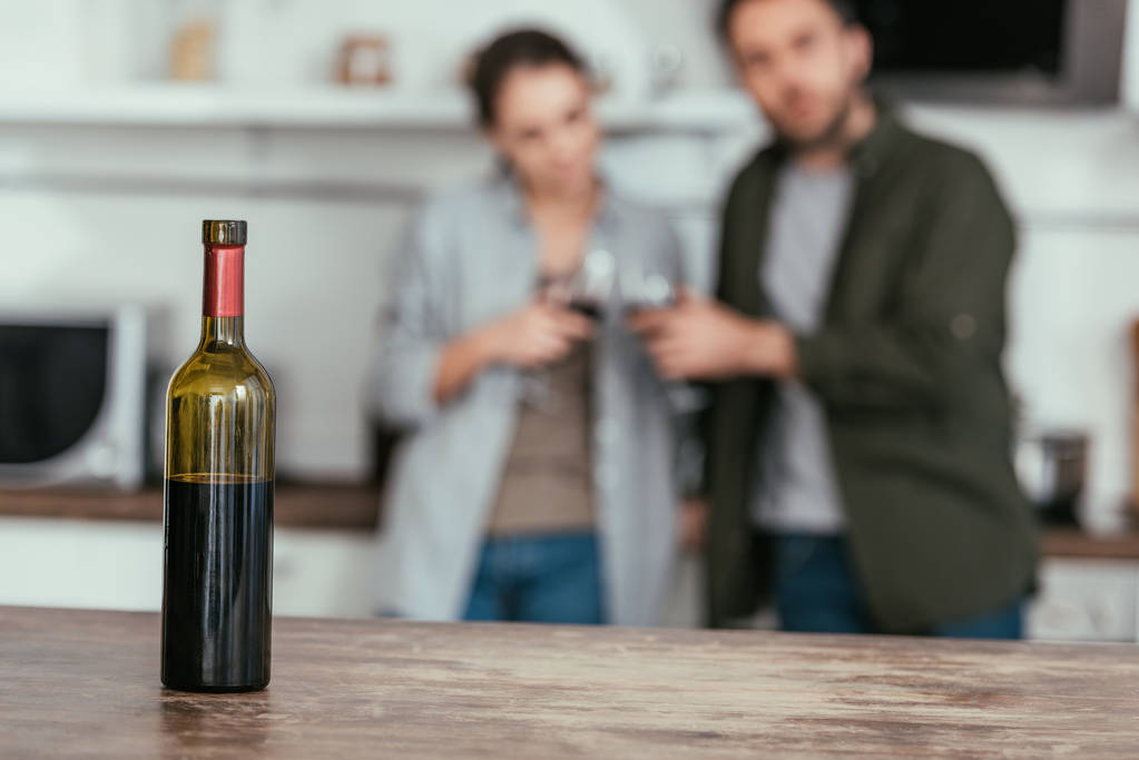 Selective focus of wine bottle on table and couple with glasses at home - Photo, Image