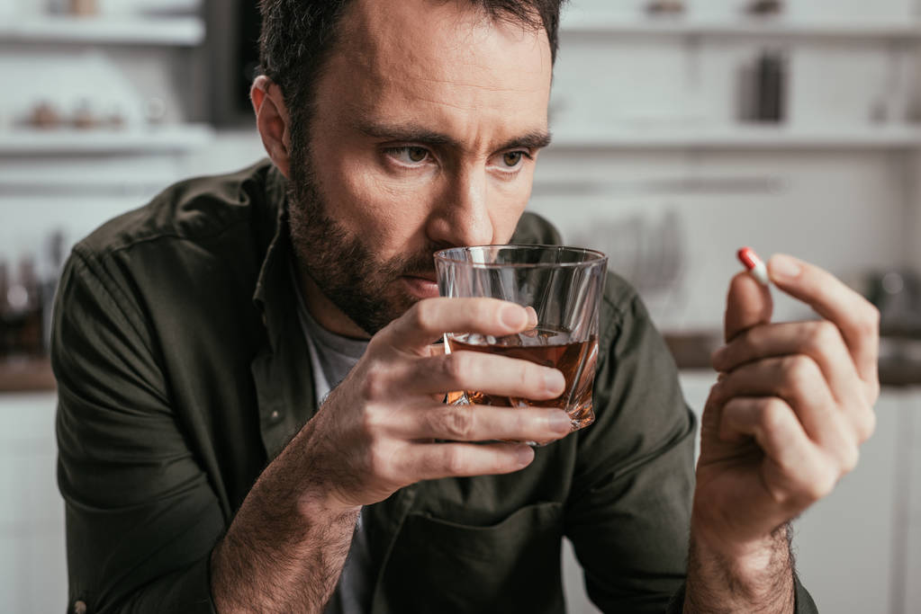 Selective focus of man with alcohol depended holding whiskey glass and pill - 写真・画像