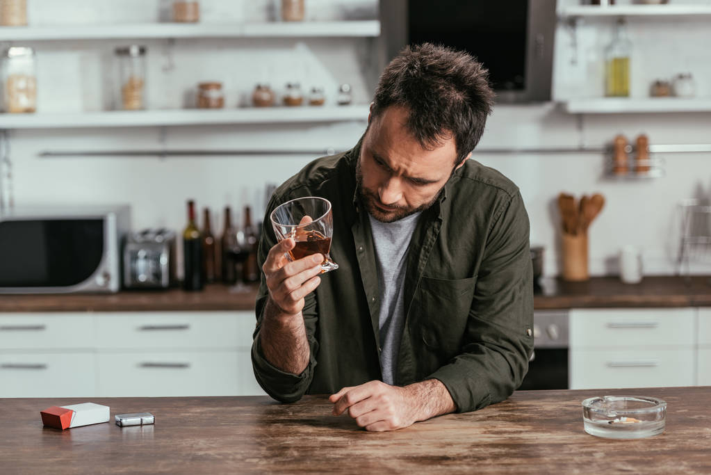 Besorgter alkoholabhängiger Mann hielt Whiskey-Glas in Küche - Foto, Bild