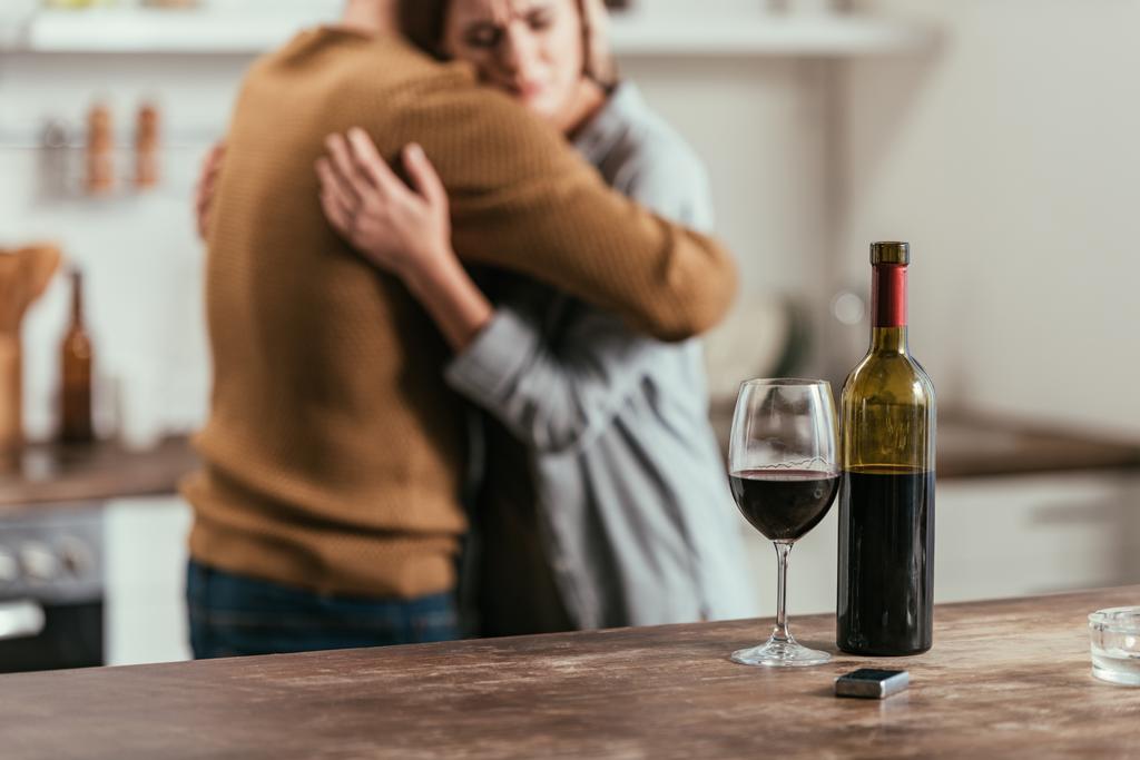 Selective focus of wine bottle and glass on table and hugging couple at background - Photo, Image