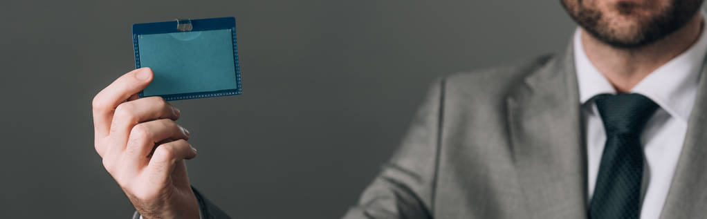 Vista cortada de homem de terno segurando crachá isolado em cinza, tiro panorâmico
 - Foto, Imagem