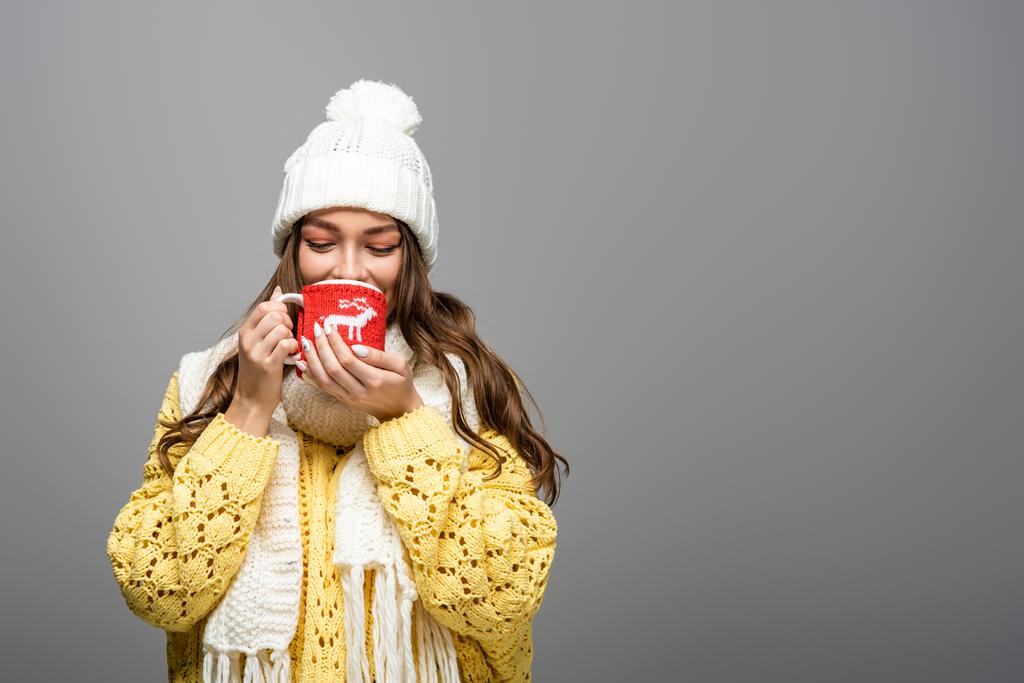 happy girl in yellow sweater, scarf, hat drinking cocoa on grey - Photo, Image
