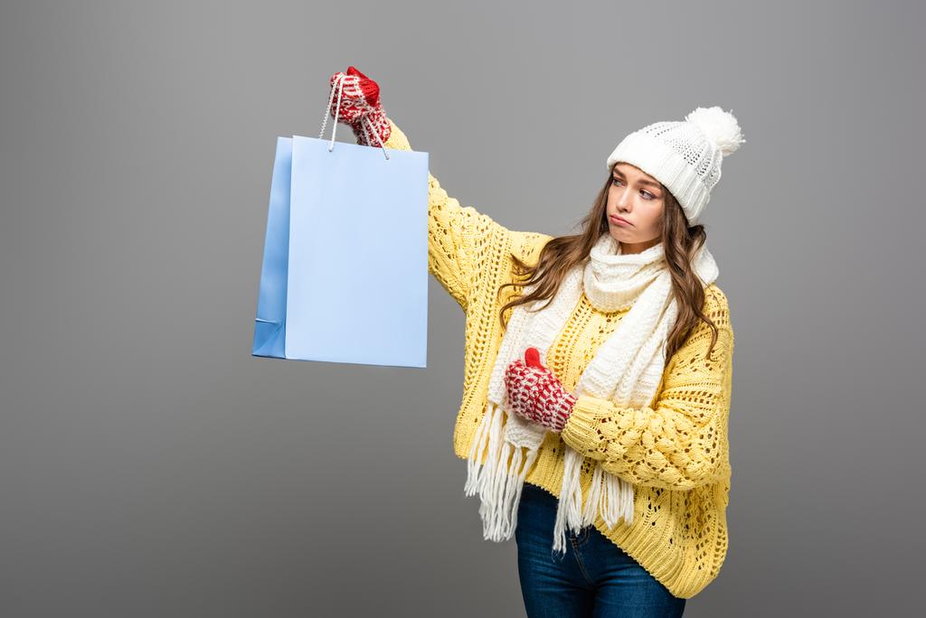 sad woman in winter outfit with shopping bag on grey background - Photo, Image