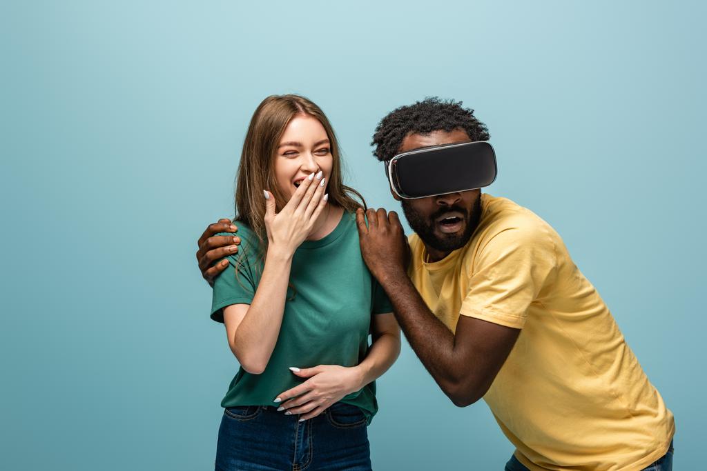 ridere ragazza in piedi vicino spaventato africano americano fidanzato in vr headset su sfondo blu
 - Foto, immagini