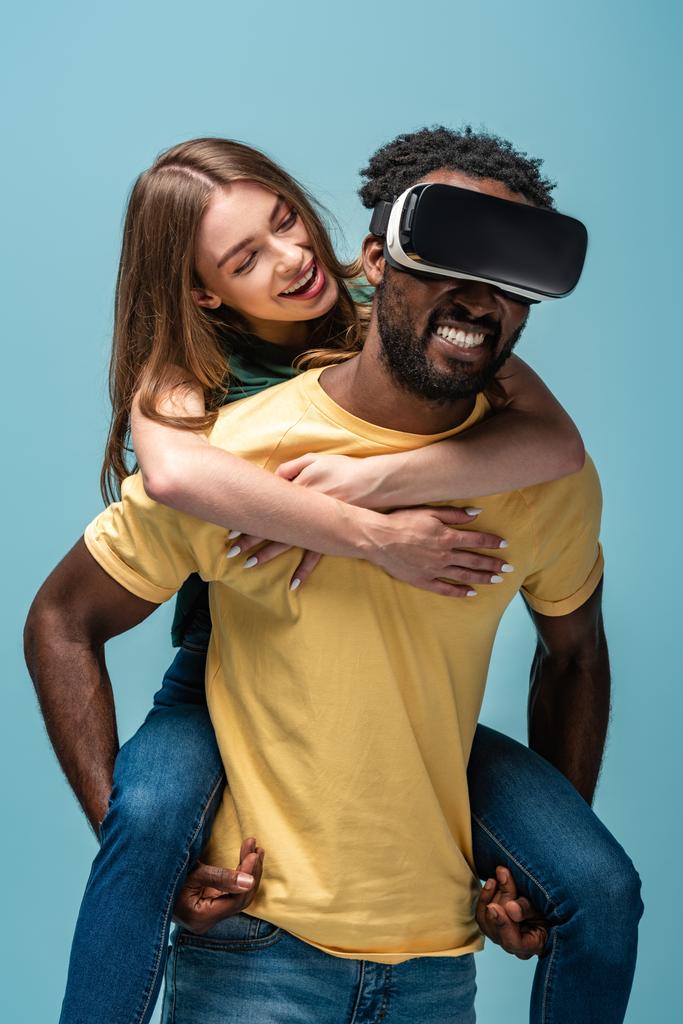 glückliches Mädchen huckepack auf afrikanisch-amerikanischen Freund in vr Headset isoliert auf blau - Foto, Bild