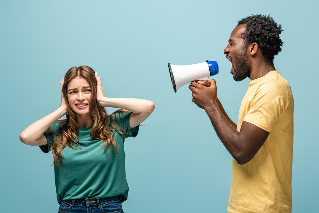 arrabbiato africano americano uomo urlando in megafono a fidanzata coprendo le orecchie con le mani su sfondo blu
 - Foto, immagini