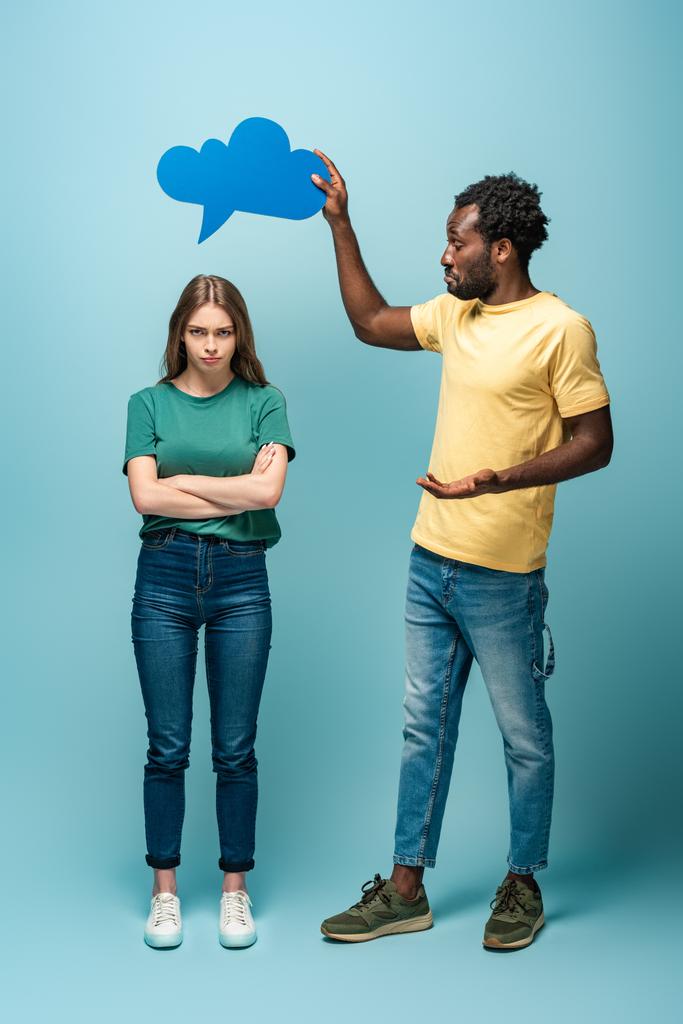 Afrikanisch-amerikanischer Mann hält Gedankenblase über beleidigter Freundin auf blauem Hintergrund - Foto, Bild