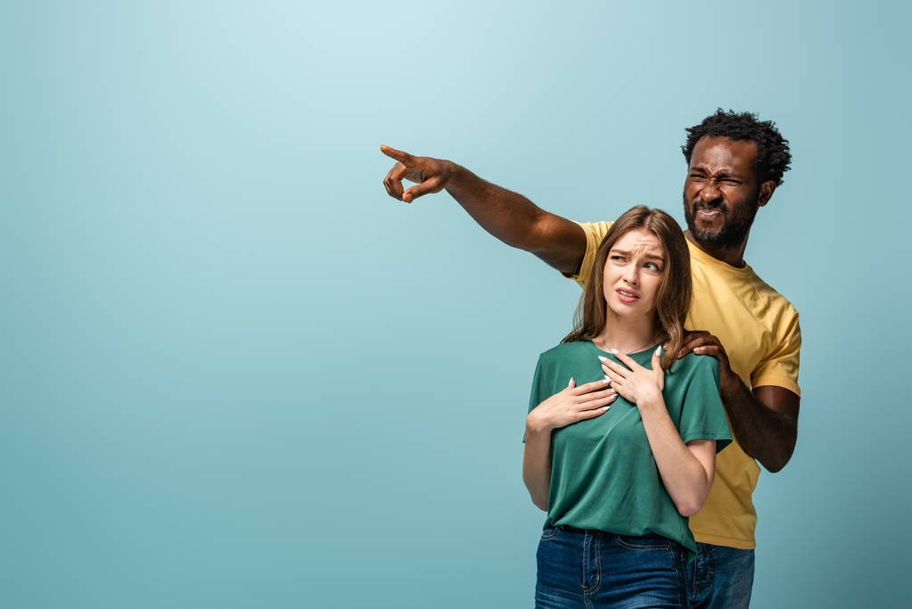 confused interracial couple pointing with finger away on blue background - Photo, Image