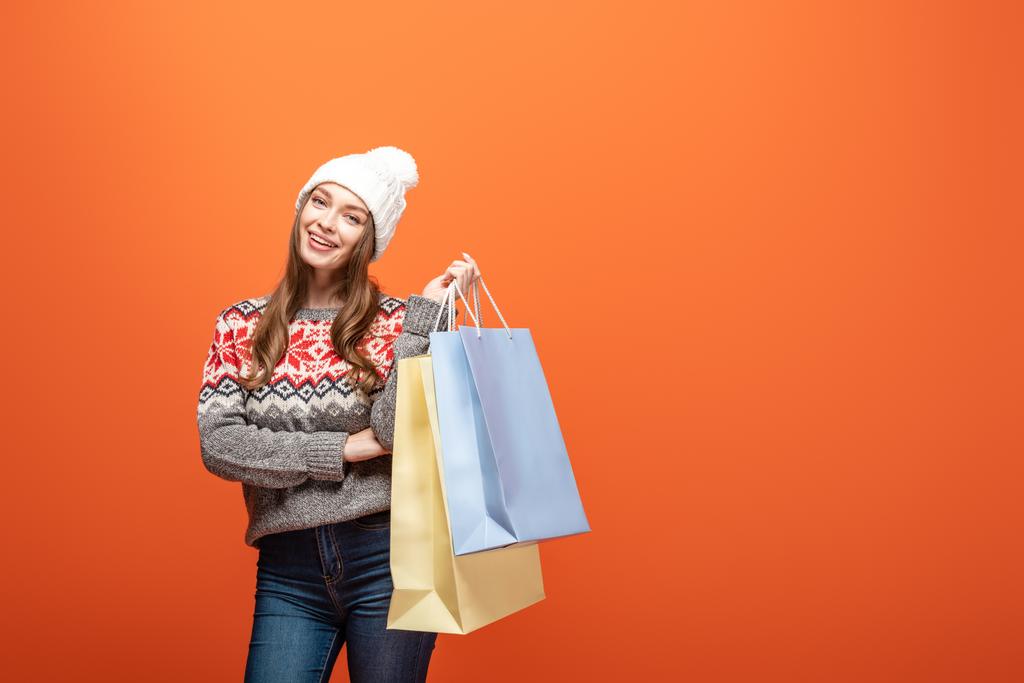 щаслива дівчина в зимовому вбранні тримає сумки на помаранчевому фоні
 - Фото, зображення