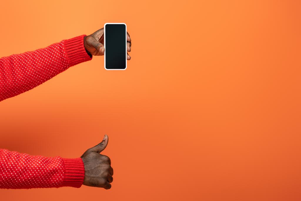 vista recortada del hombre afroamericano sosteniendo el teléfono inteligente y mostrando el pulgar hacia arriba sobre fondo naranja
 - Foto, imagen