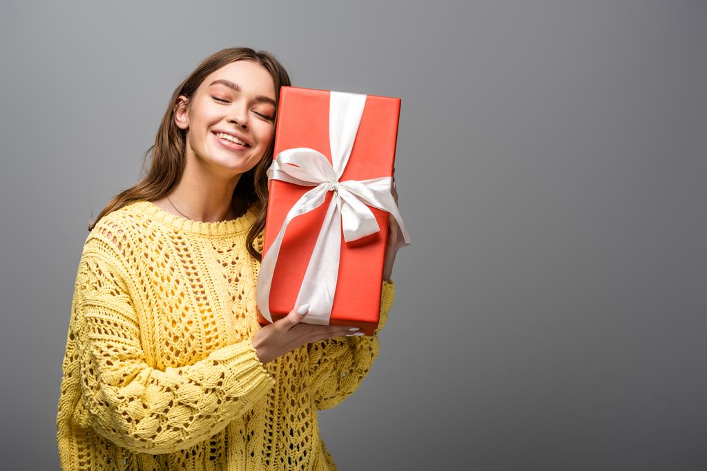 pleased woman in yellow sweater holding gift box on grey background - Photo, Image