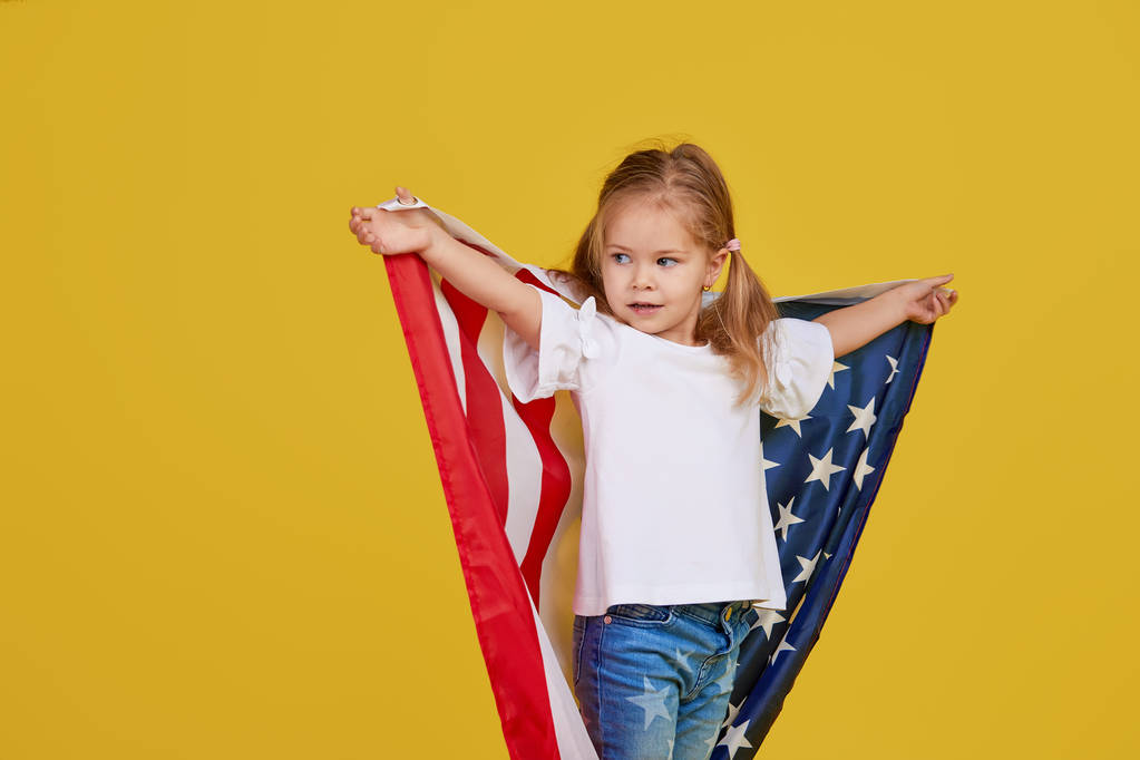 Vacanza patriottica. Bambino felice, carina bambina con bandiera americana su sfondo giallo studio. Gli Stati Uniti festeggiano il 4 luglio, giorno dell'indipendenza
. - Foto, immagini