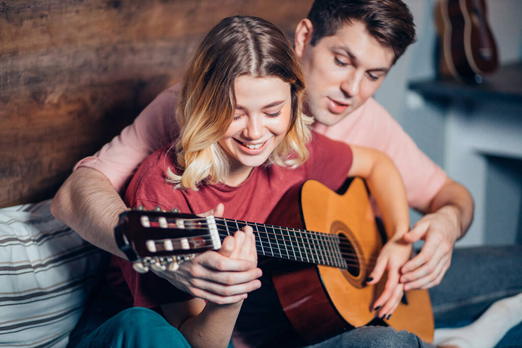 Ωραίο ζευγάρι ξεκουράζεται στο σπίτι και παίζει κιθάρα. - Φωτογραφία, εικόνα