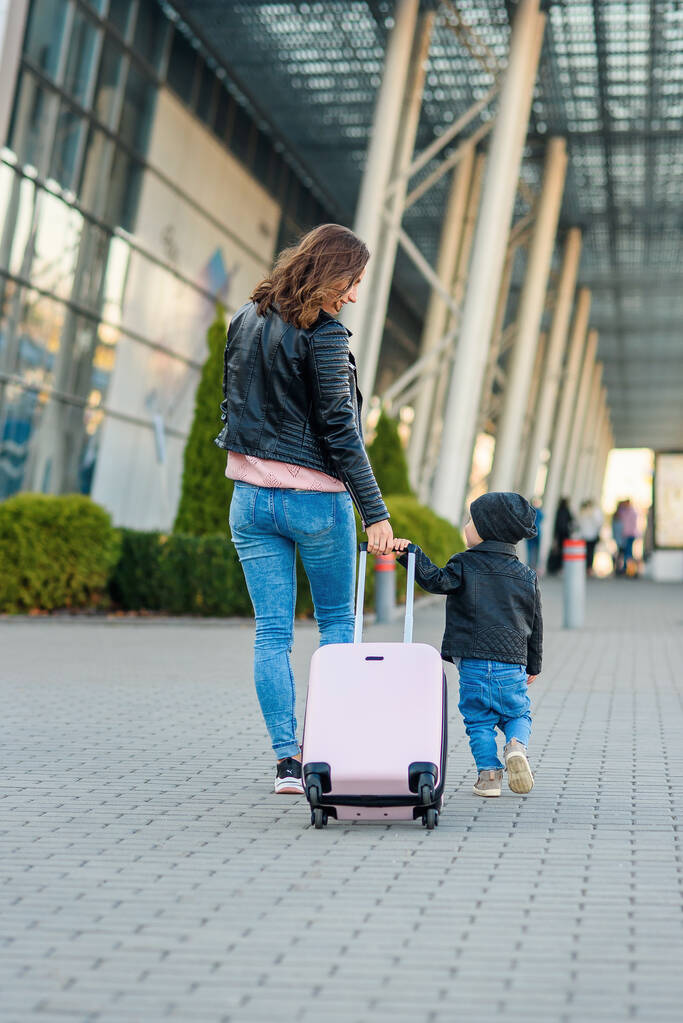 Beautiful mother and her stylish cute daughter walk together and pull a pink suitcase to the airport. - Photo, Image
