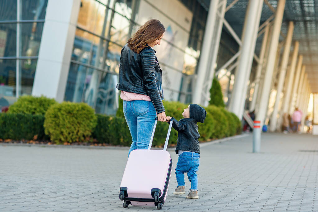 Kaunis äiti ja hänen tyylikäs söpö tyttärensä kävelevät yhdessä ja vetävät vaaleanpunaisen matkalaukun lentokentälle
. - Valokuva, kuva