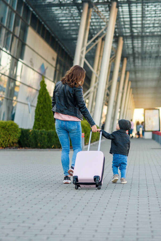 Мать и ее стильная симпатичная дочь гуляют вместе и тащат розовый чемодан в аэропорт
. - Фото, изображение