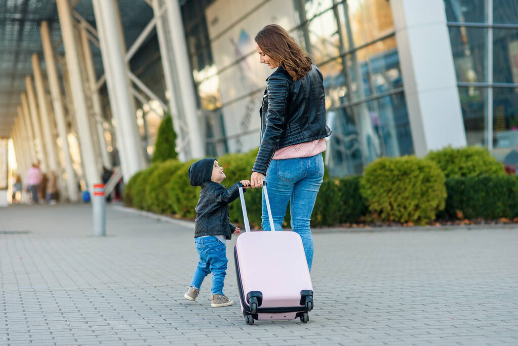 Belle mère et sa fille mignonne élégante marchent ensemble et tirent une valise rose à l'aéroport
. - Photo, image