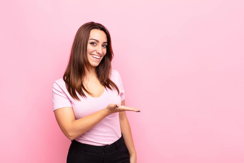 молода красива жінка весело посміхається, відчуває себе щасливою і показує концепцію в копіювальному просторі з долонею руки проти рожевої стіни
 - Фото, зображення