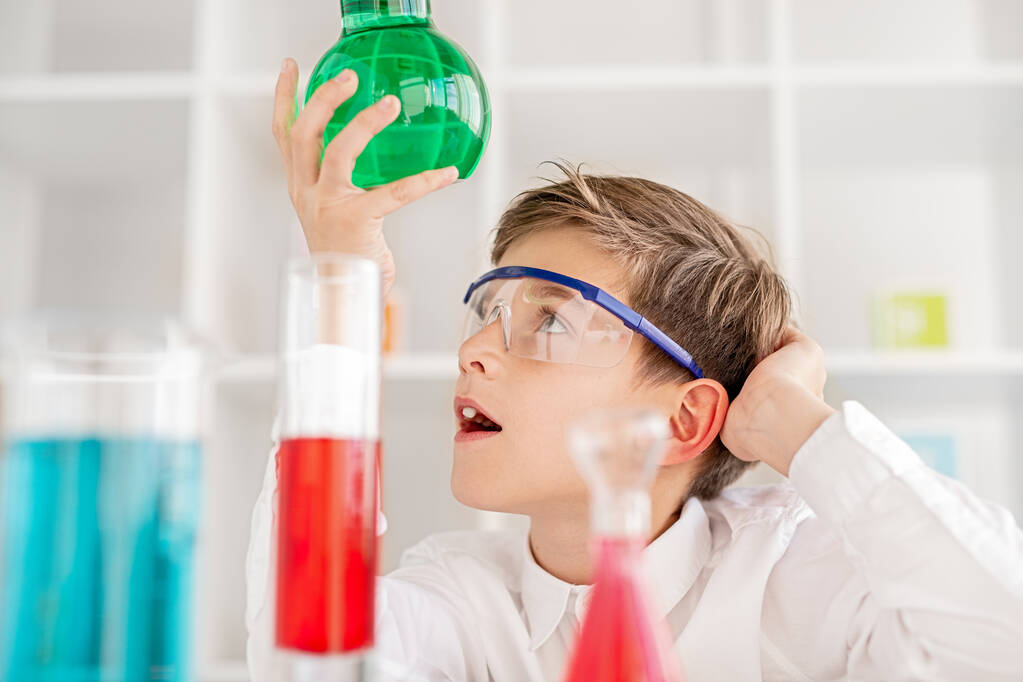 Verbaasde jongen die de chemische stof in een kolf onderzoekt - Foto, afbeelding