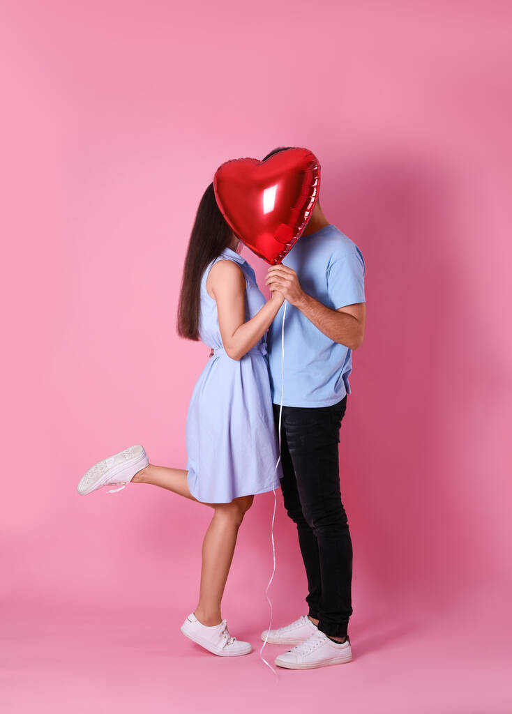 Joli couple caché derrière un ballon en forme de coeur sur fond rose. Fête de la Saint Valentin
 - Photo, image