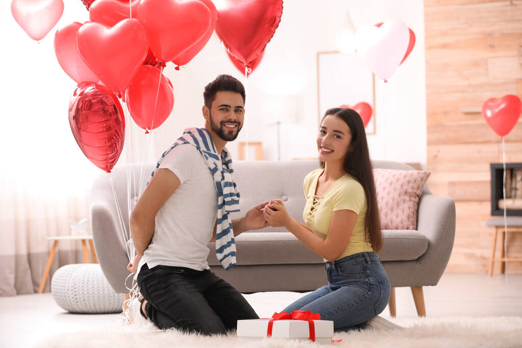 Šťastný mladý pár s balónky ve tvaru srdce v obývacím pokoji. Valentýnská oslava - Fotografie, Obrázek