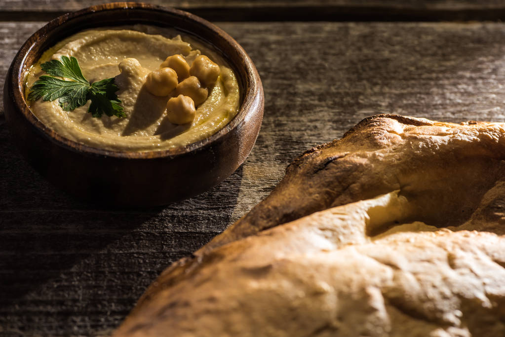 delicioso hummus com grão de bico em tigela perto de pita cozido na mesa rústica de madeira
 - Foto, Imagem