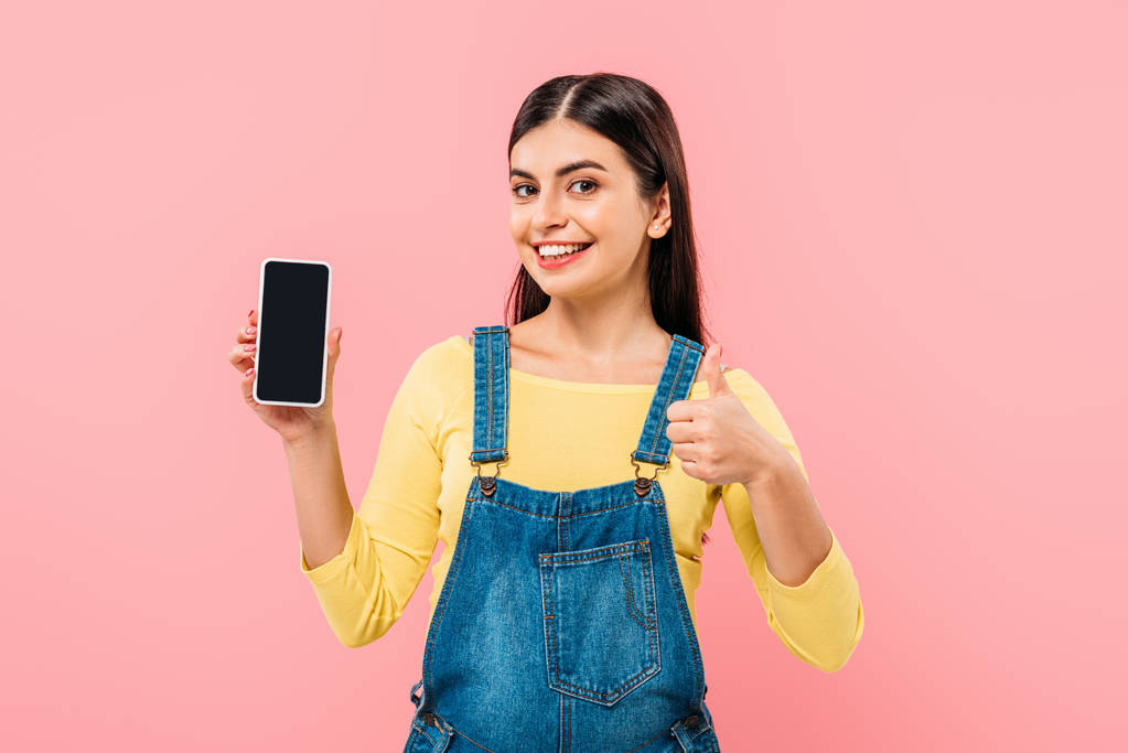 mosolygós terhes csinos lány gazdaság okostelefon üres képernyőn, és mutatja hüvelykujját fel elszigetelt rózsaszín - Fotó, kép