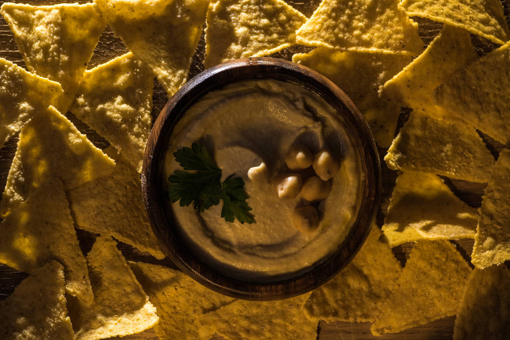 верхний вид на вкусный хумус с горохом в миске возле начос
 - Фото, изображение