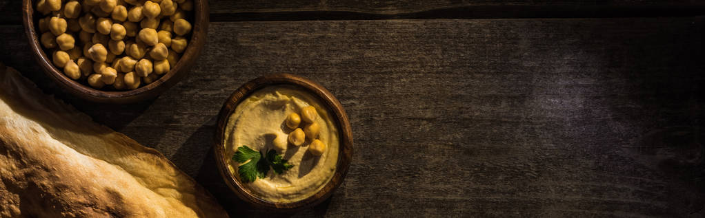 vista superior del delicioso hummus con garbanzos en un tazón cerca de pita recién horneada sobre una mesa rústica de madera, plano panorámico
 - Foto, Imagen