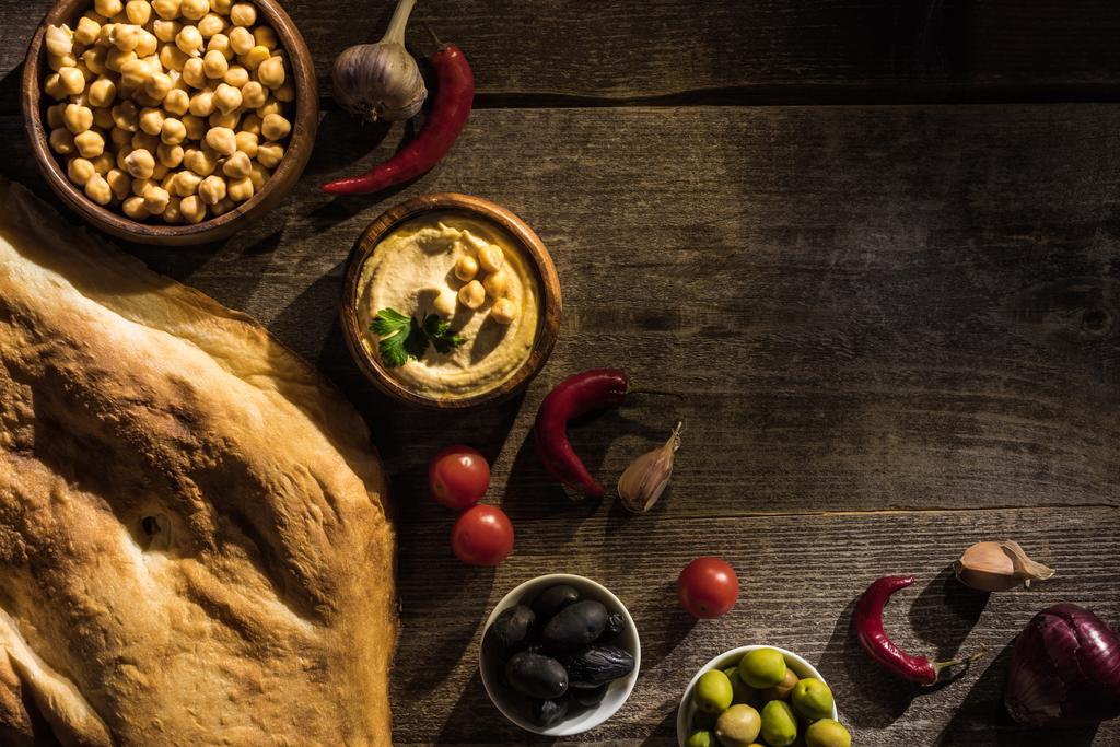 vista superior de delicioso hummus, grão de bico, pita, especiarias e azeitonas em mesa rústica de madeira
 - Foto, Imagem