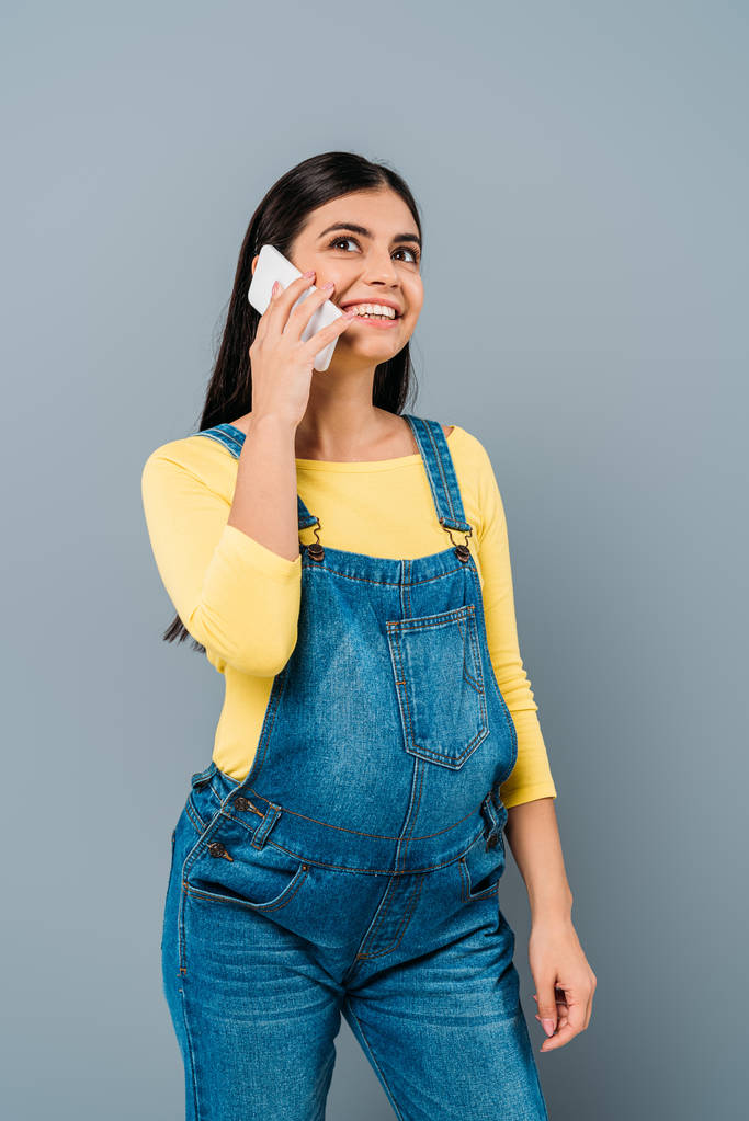 улыбающаяся беременная красивая девушка разговаривающая на смартфоне изолированная от серых
 - Фото, изображение
