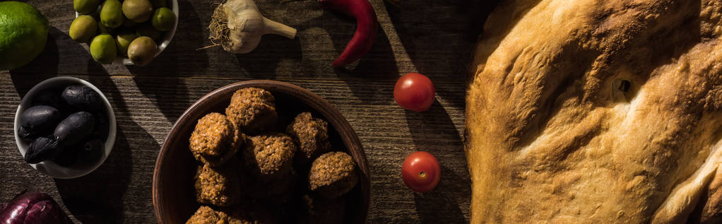 vista superior de delicioso falafel, hummus, pita, legumes e azeitonas em mesa rústica de madeira, tiro panorâmico
 - Foto, Imagem