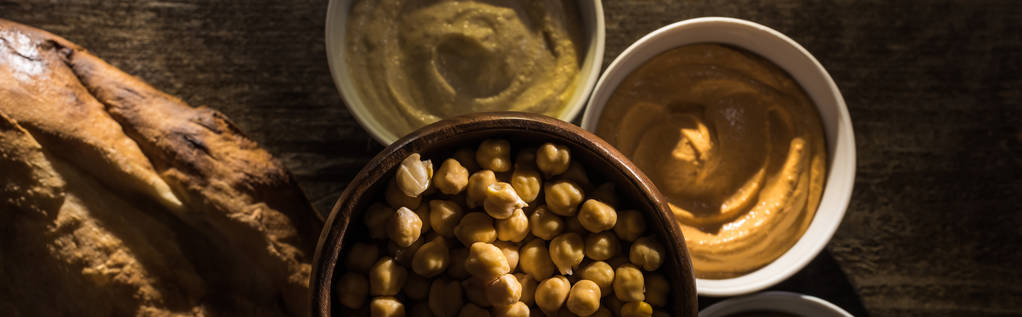 top view of delicious assorted hummus, chickpeas and fresh baked pita on wooden rustic table, panoramic shot - Photo, Image