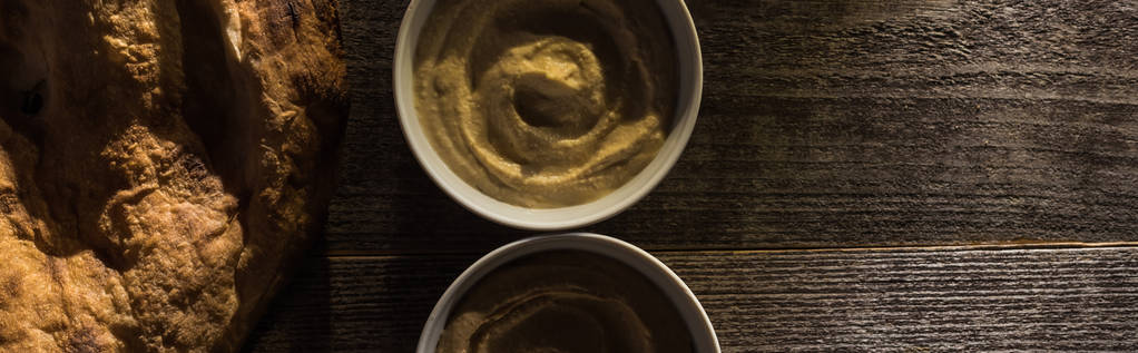 Draufsicht auf köstlich sortierten Hummus und frisch gebackene Pita auf rustikalem Holztisch, Panoramaaufnahme - Foto, Bild