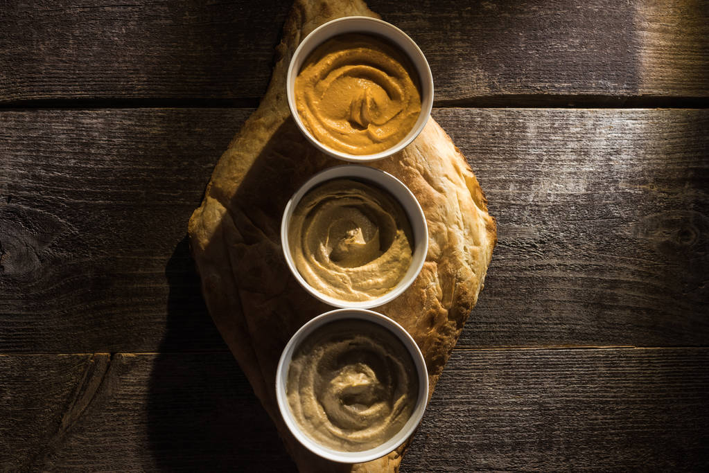 верхний вид вкусного разнообразного хумуса на свежей запечённой пите на деревянном деревенском столе
 - Фото, изображение