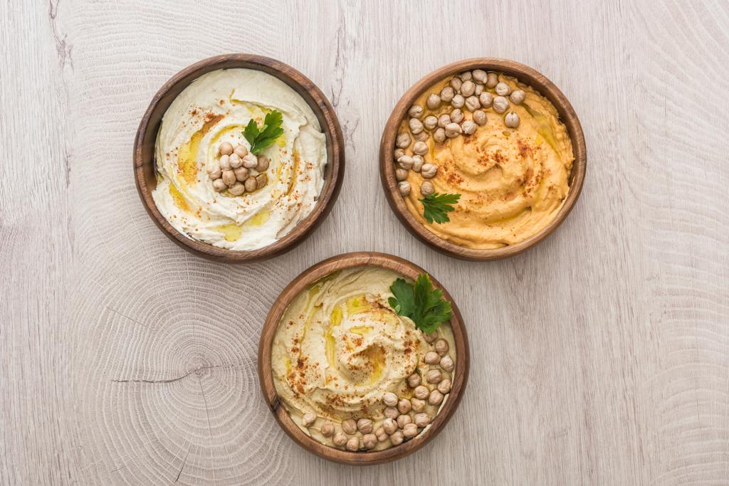 top view of delicious hummus with chickpeas in bowls on beige wooden table - Photo, Image