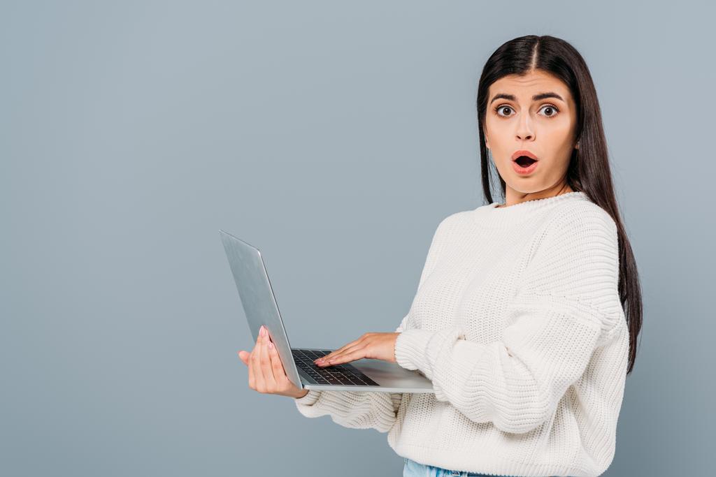 shocked pretty girl in white sweater using laptop isolated on grey - Photo, Image