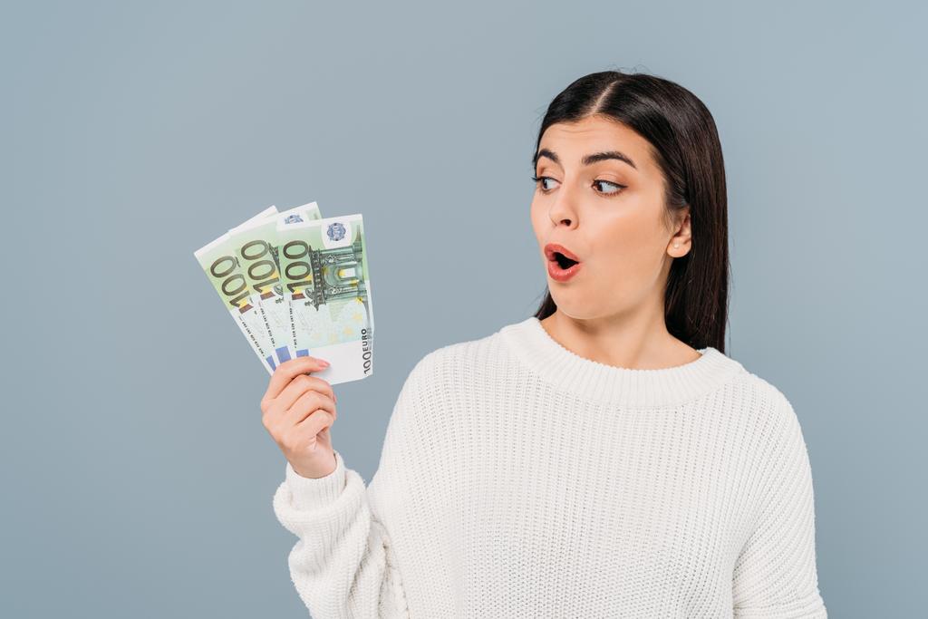 shocked pretty girl in white sweater looking at euro banknotes isolated on grey - Photo, Image