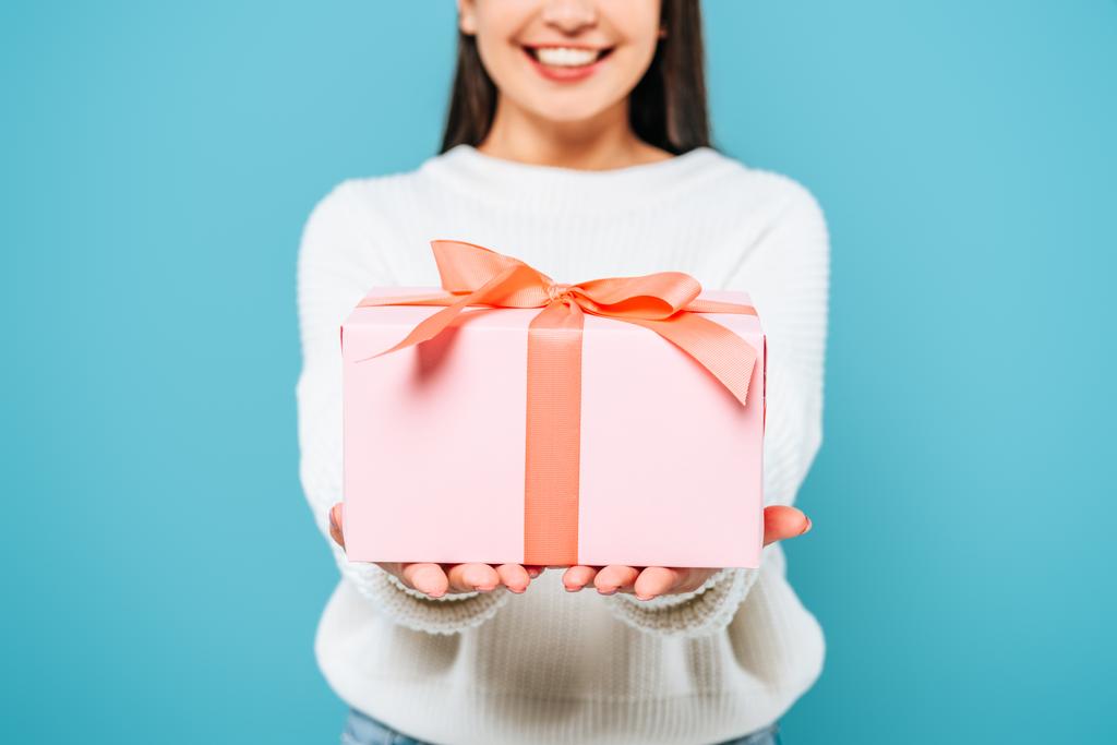 обрезанный вид улыбающейся красивой девушки в белом свитере с подарочной коробкой, изолированной на голубом
 - Фото, изображение