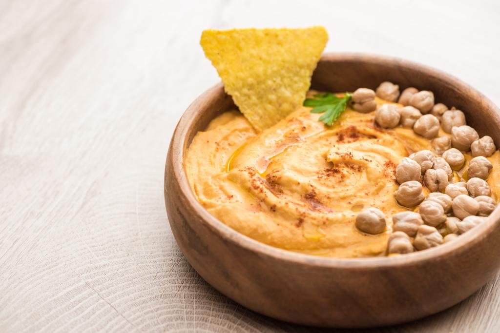vista de perto do delicioso hummus com grão de bico e nacho na tigela na mesa de madeira bege
 - Foto, Imagem