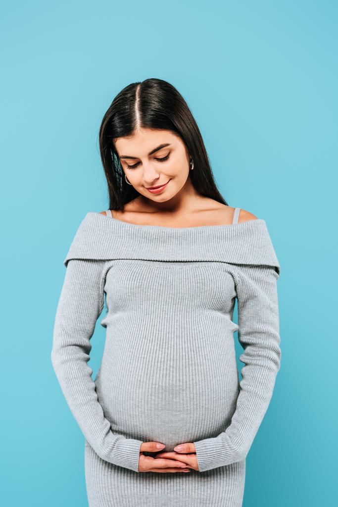 Lächeln schwangeres hübsches Mädchen berührt Bauch isoliert auf blau - Foto, Bild
