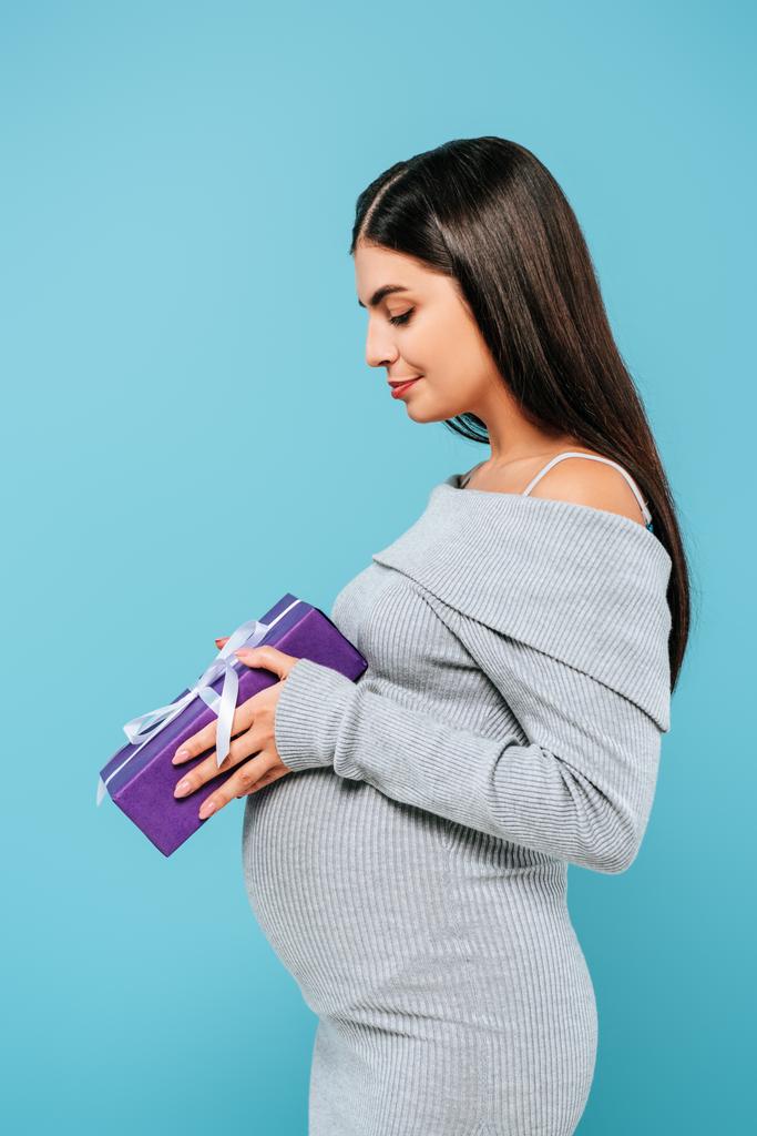 Seitenansicht von schwangeren hübschen Mädchen hält Geschenke isoliert auf blau - Foto, Bild