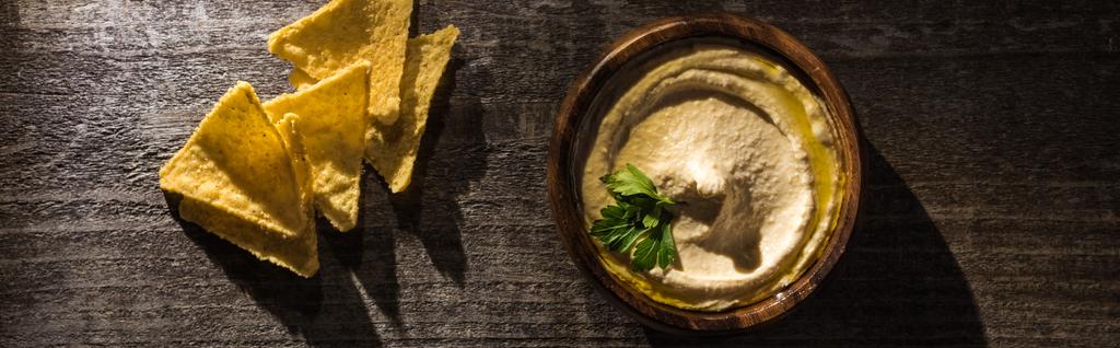 Draufsicht auf köstlichen Hummus mit Mais-Nachos auf rustikalem Holztisch, Panoramaaufnahme - Foto, Bild